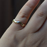 A close-up of a hand wearing a wavy, organic-shaped gold ring.
