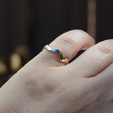 A close-up of a hand wearing a slim, wavy band ring with a two-tone finish of yellow gold and silver, set against a dark, blurred background.