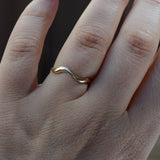 A close-up of a hand wearing a thin, wavy two-tone ring with gold and silver metals, set against a dark, blurred background.