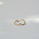 A single gold wavy band ring resting on a plain light gray surface.
