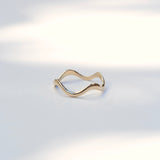 A thin, wavy gold ring with a polished finish, displayed on a clean white surface with soft, natural shadows.