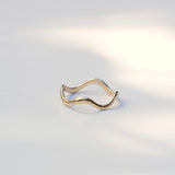 A thin, wavy gold ring with an open, flexible design, photographed on a clean white surface with soft, natural shadows.