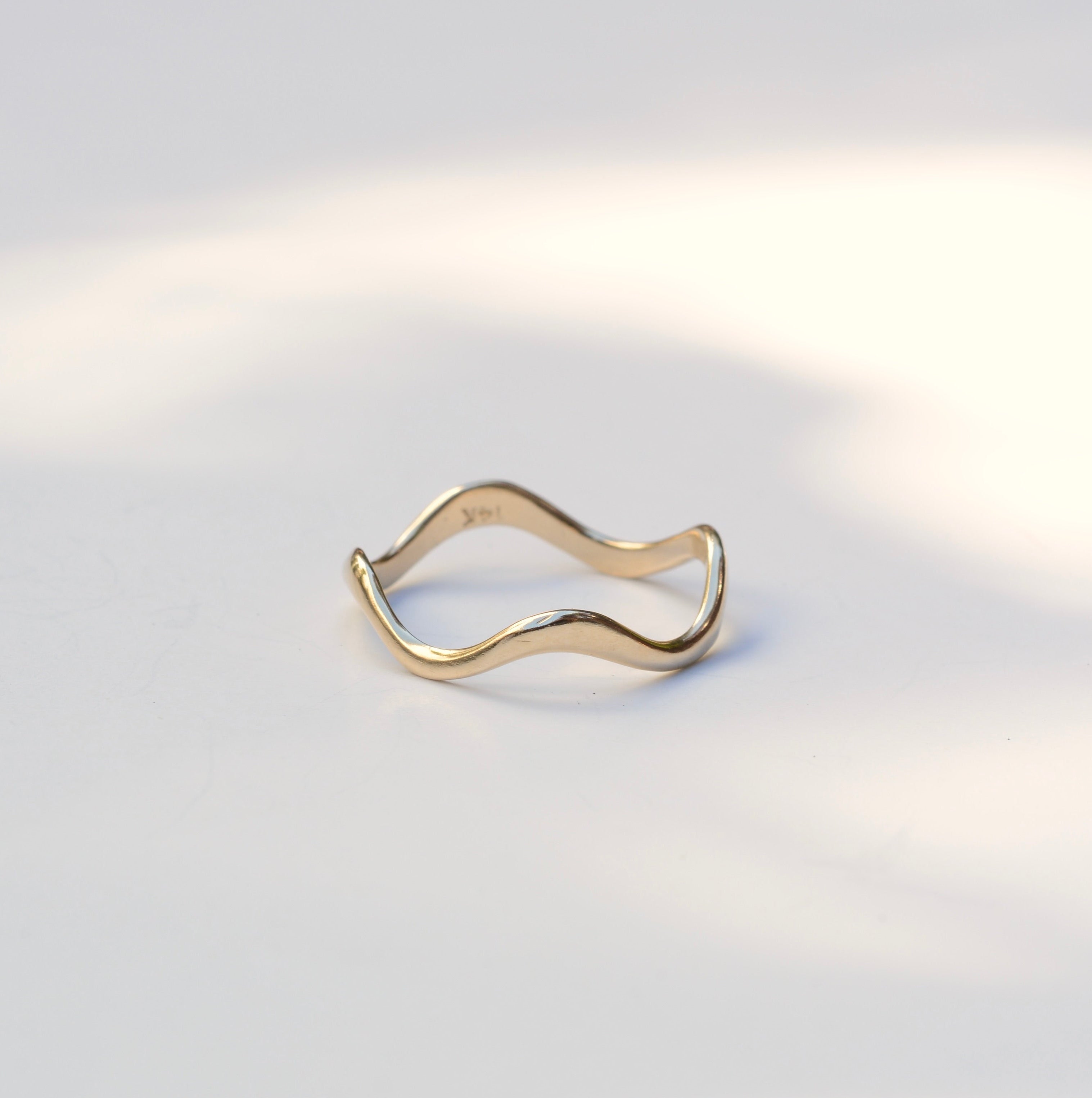 Thin wavy gold band sitting on a white background