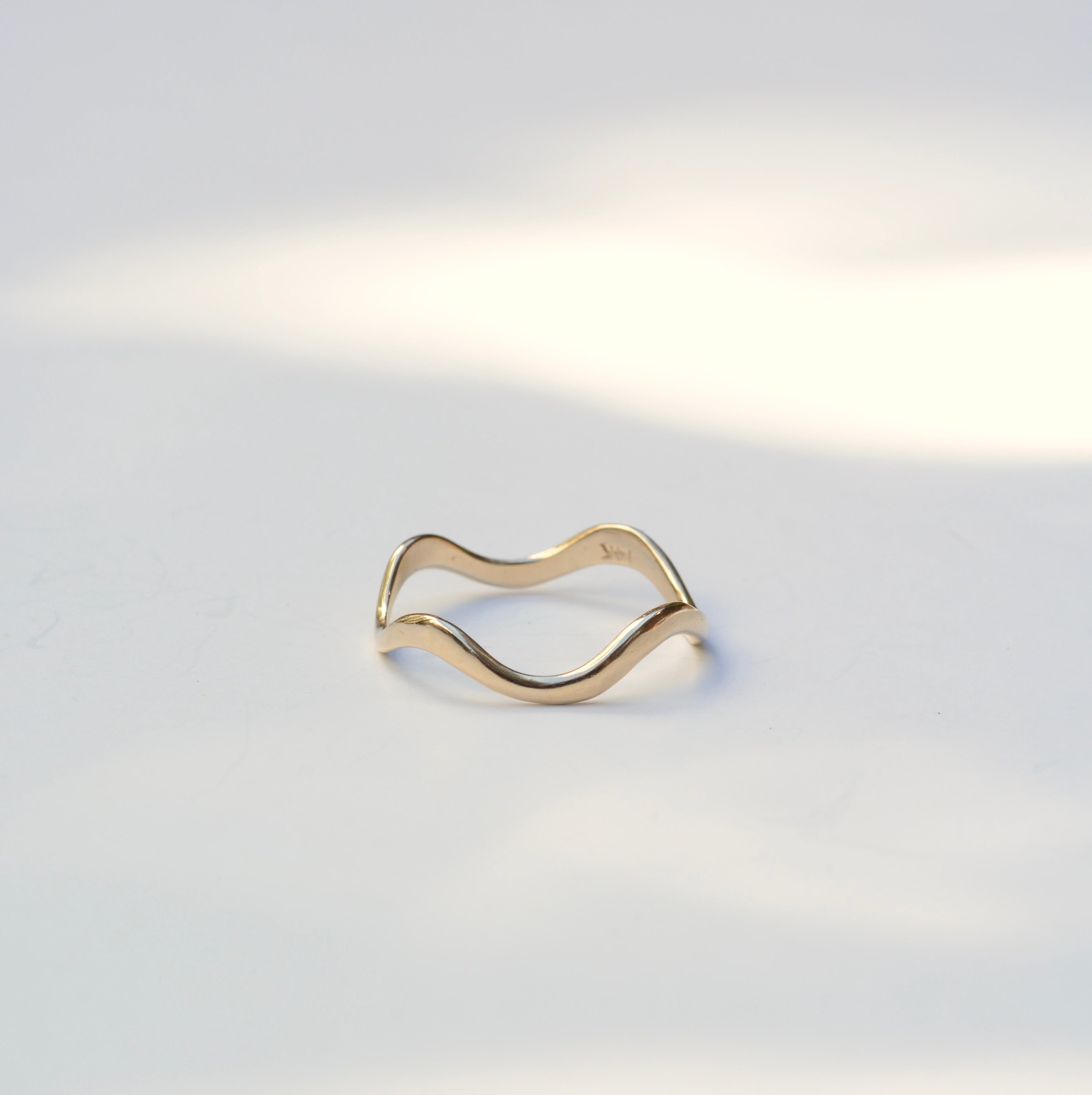 Thin 14k yellow gold ring with wavy curves sitting on a white background