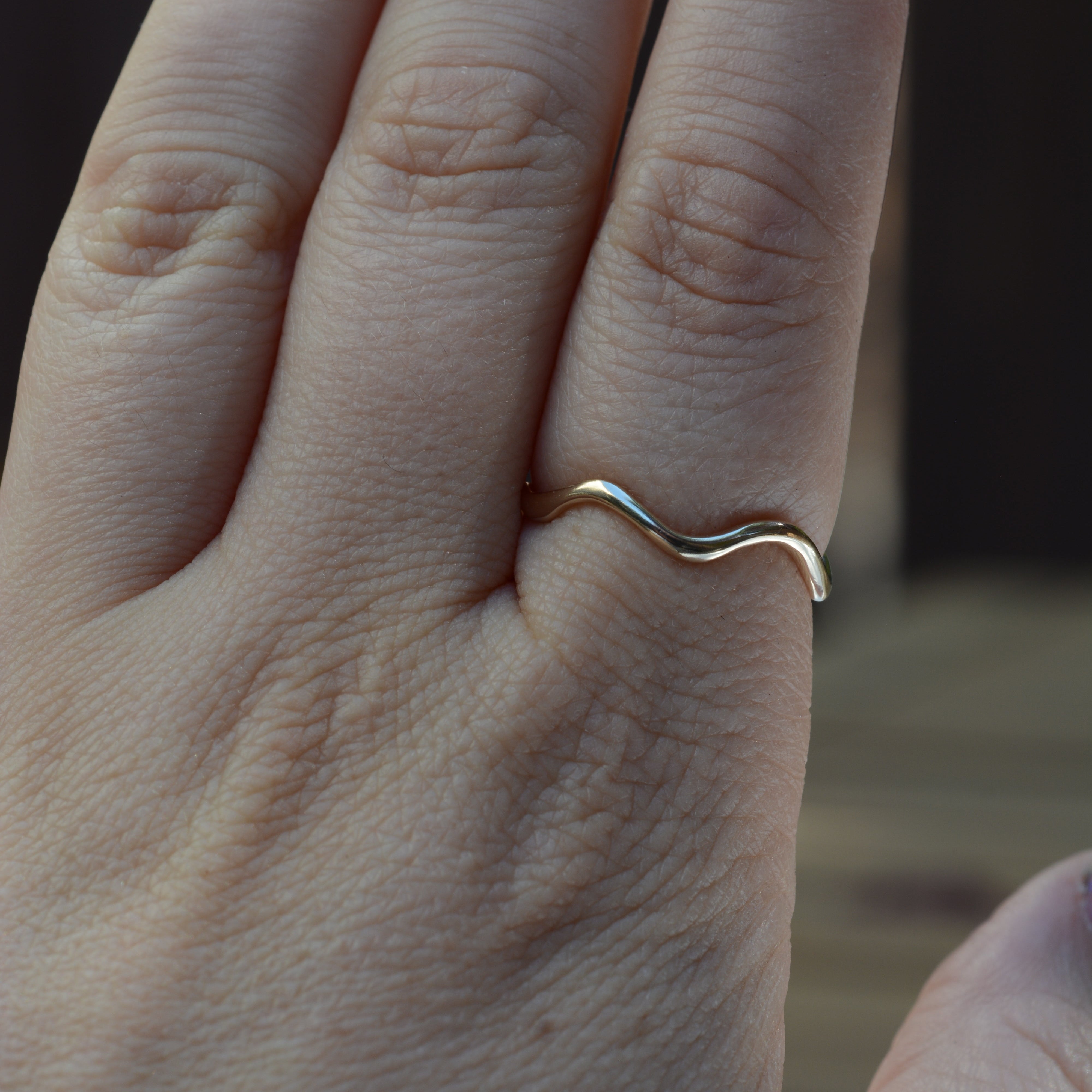 A close-up of a hand wearing a thin, wavy gold band ring on the pointer finger.