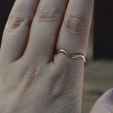 A close-up of a hand wearing a thin, wavy gold band ring on the pointer finger.
