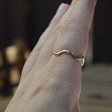 A close-up of a hand wearing a thin, wavy gold band ring against a dark, blurred background.