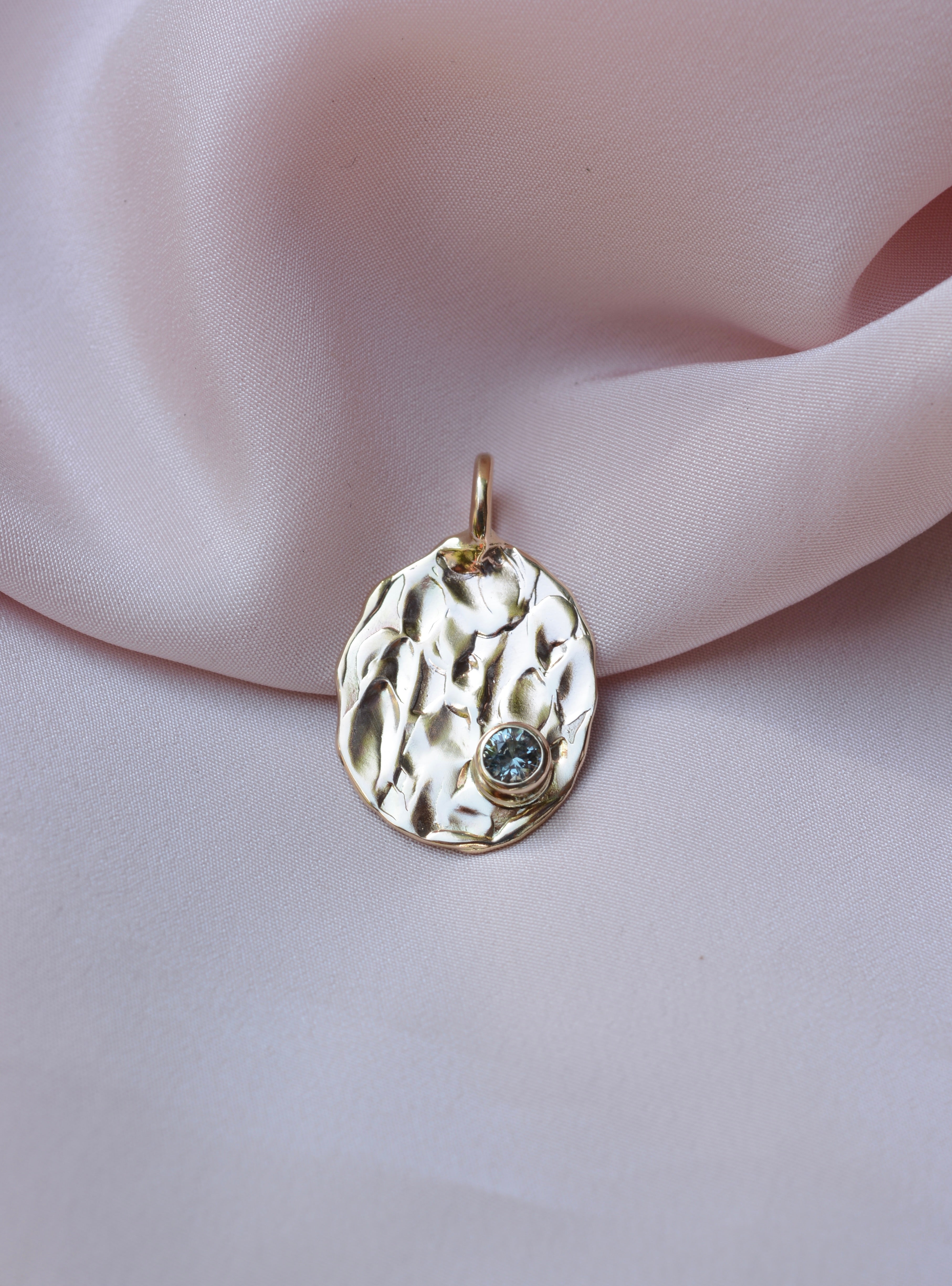Gold oval pendant with molten texture and round blue sapphire on the bottom right