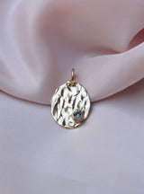 Gold oval pendant with molten texture and round blue sapphire on the bottom right