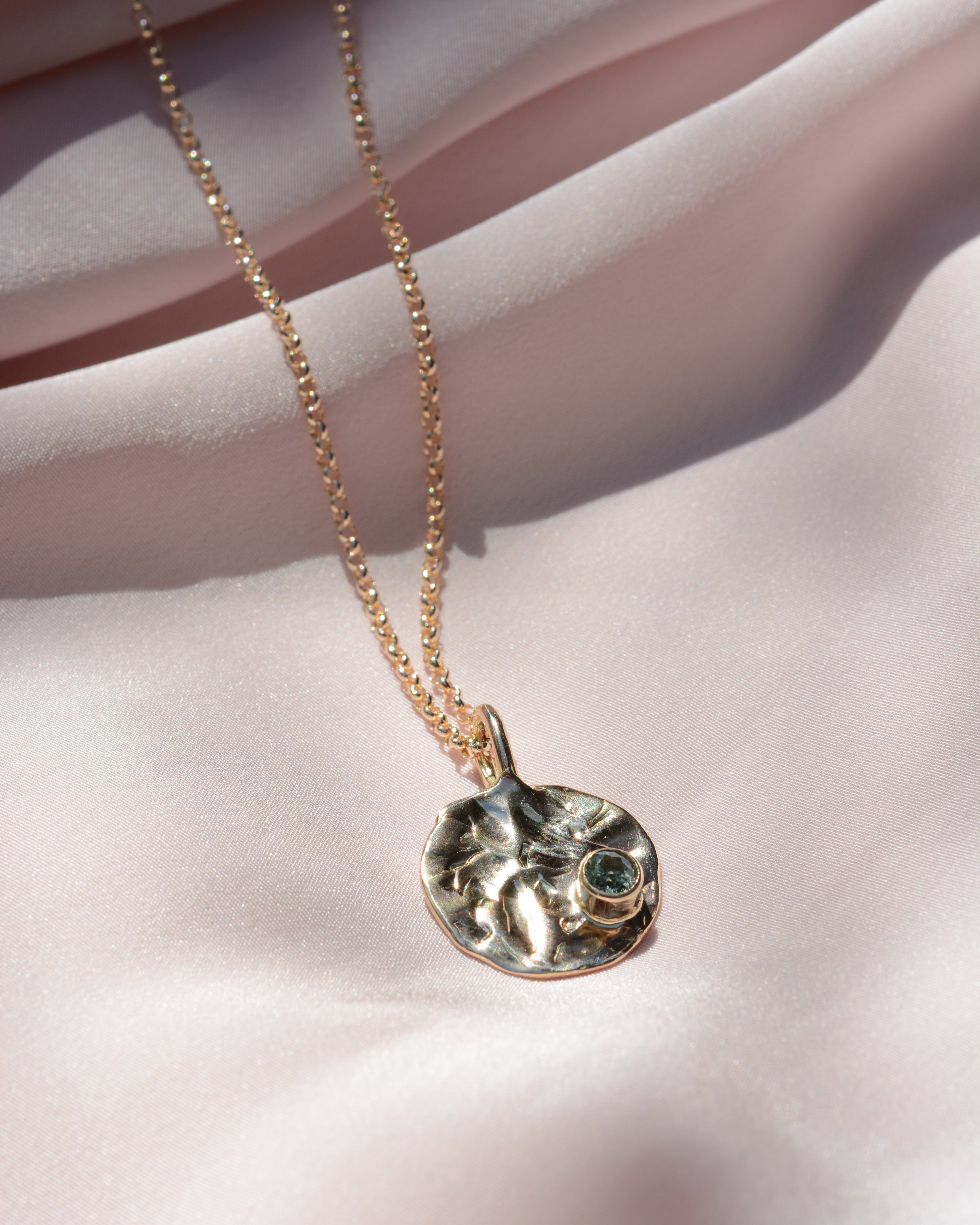 Round pendant on rolo chain with texture and blue sapphire on the bottom right corner
