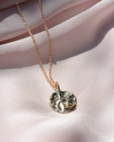 Round pendant on rolo chain with texture and blue sapphire on the bottom right corner