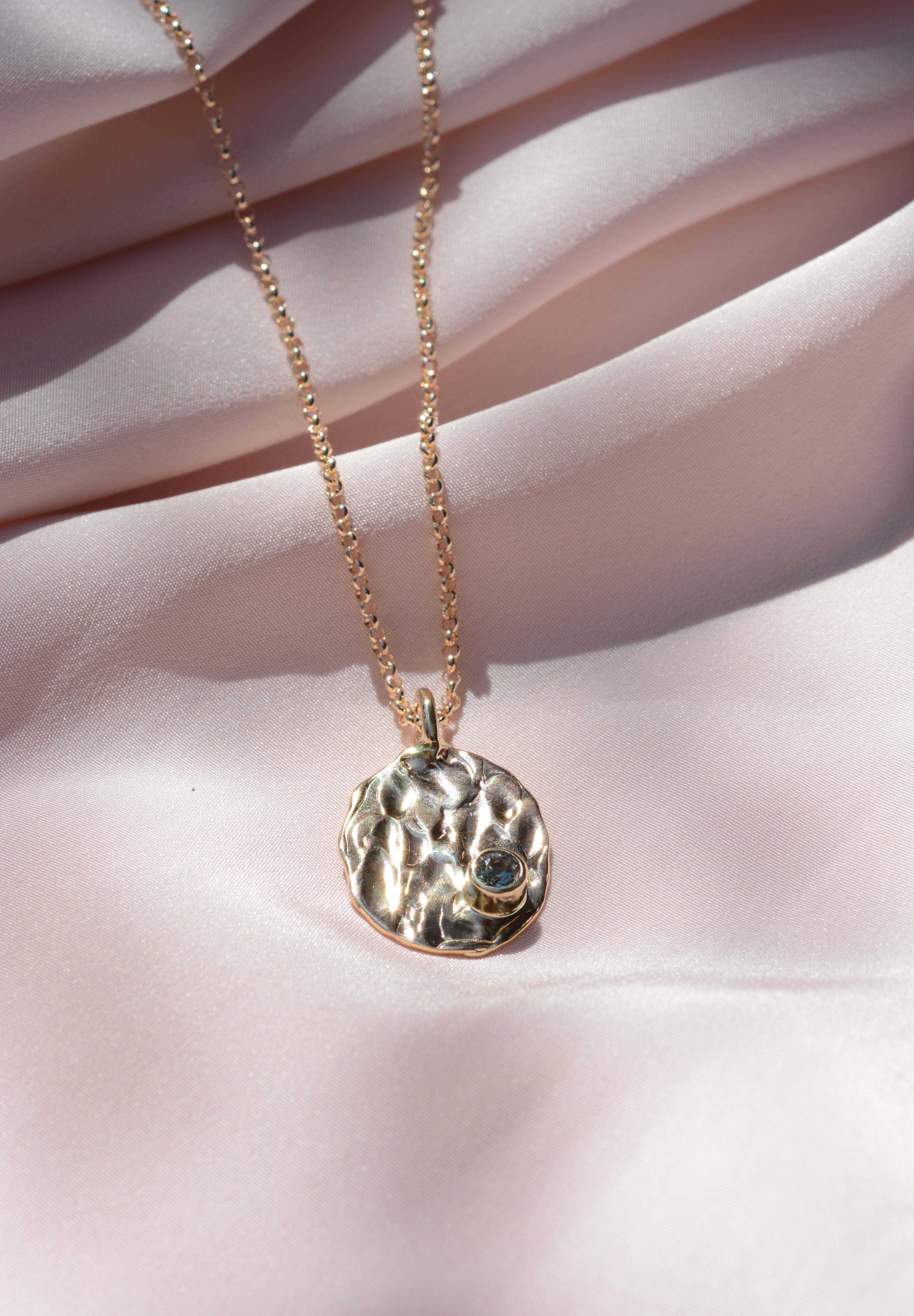 Oval, textured, pendant on a chain with a round blue sapphire on the bottom right