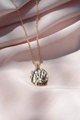Oval, textured, pendant on a chain with a round blue sapphire on the bottom right