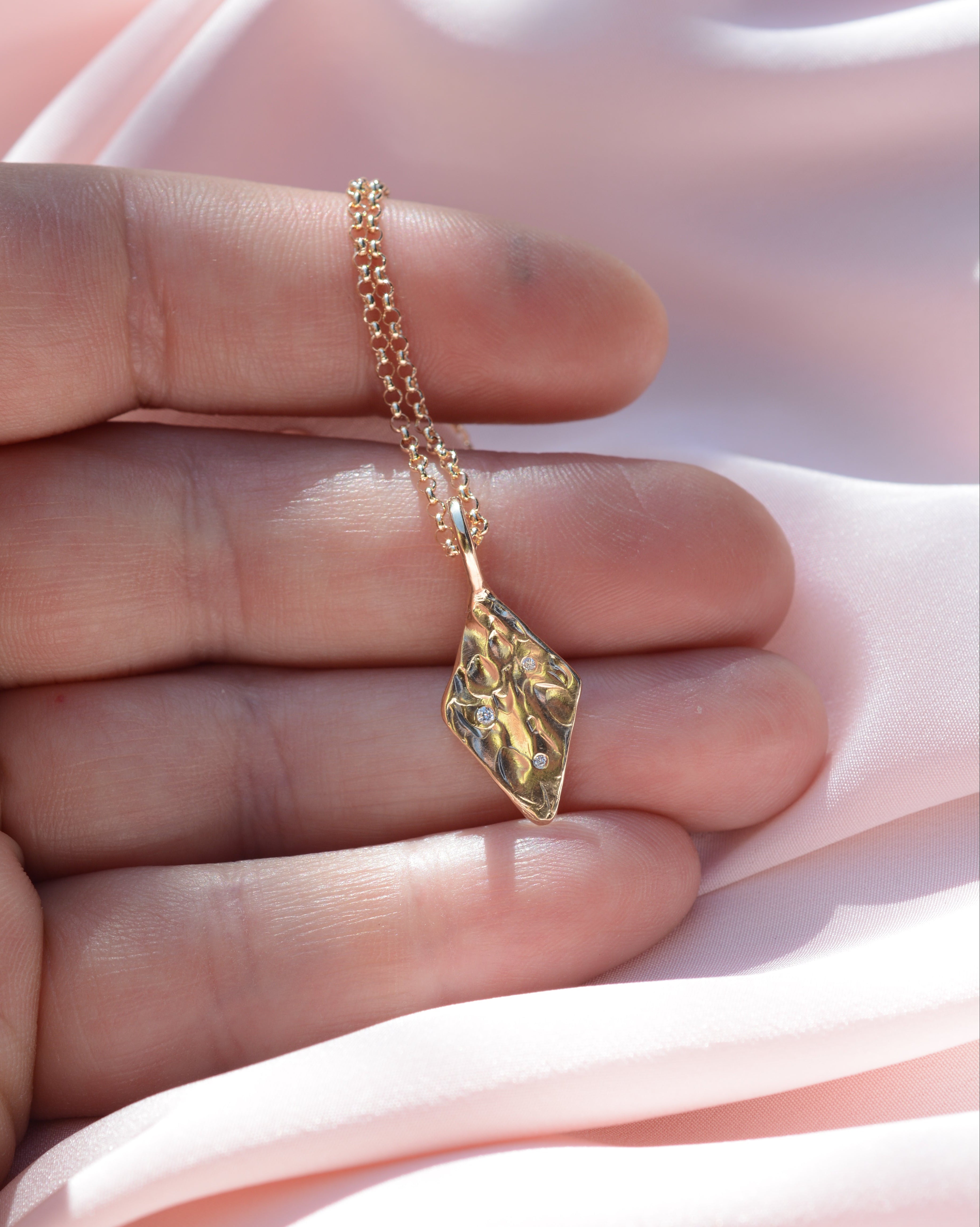 Hand holding diamond shaped pendant with organic texture and 3 flush set lab grown diamonds
