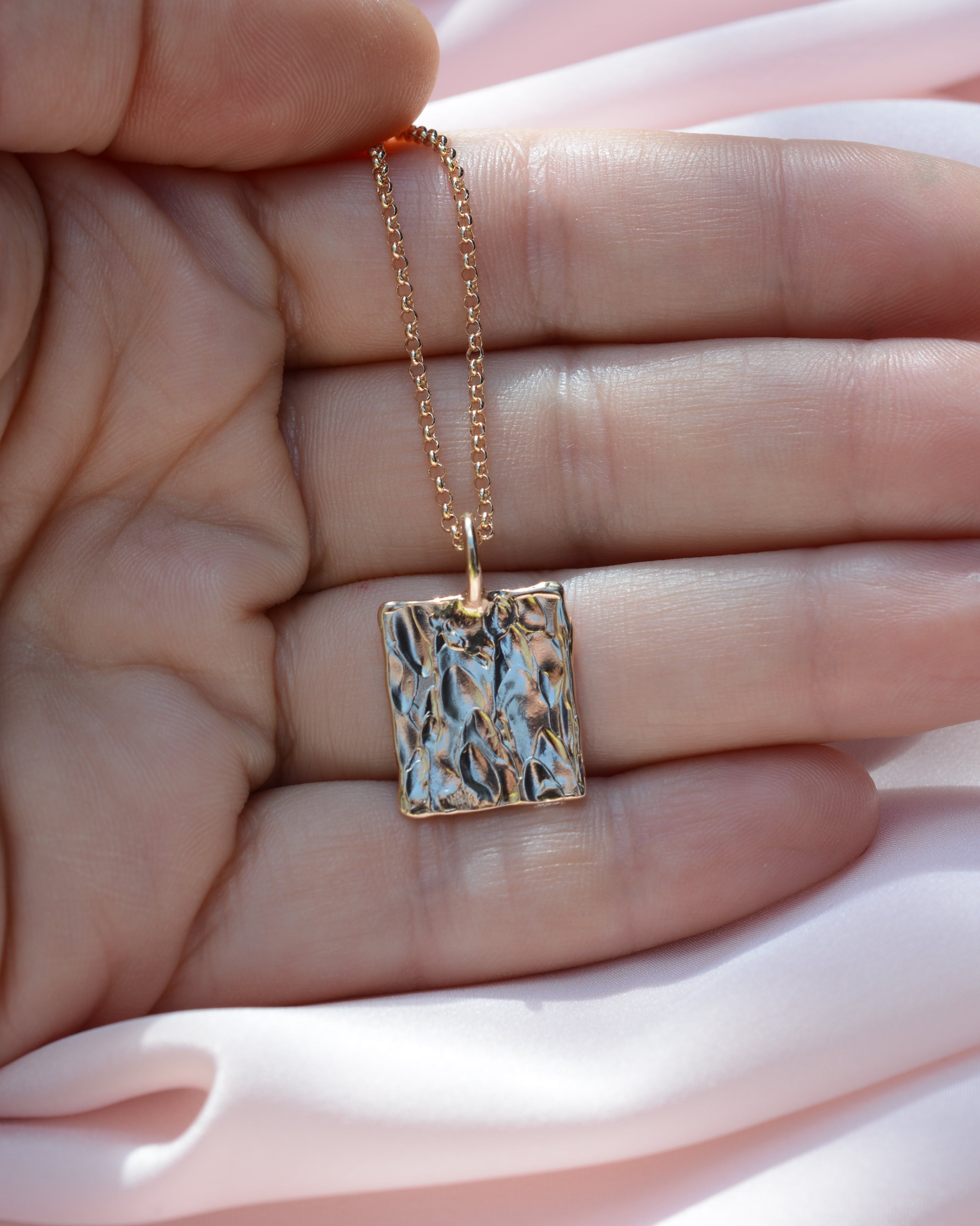 Hand holding a rectangular pendant with organic bark like texture