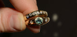 Gold ring with gemstone held between fingers against a dark background