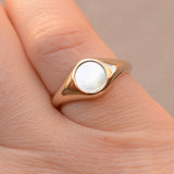 Gold signet ring with a white mother of pearl inlay stone on a beige background