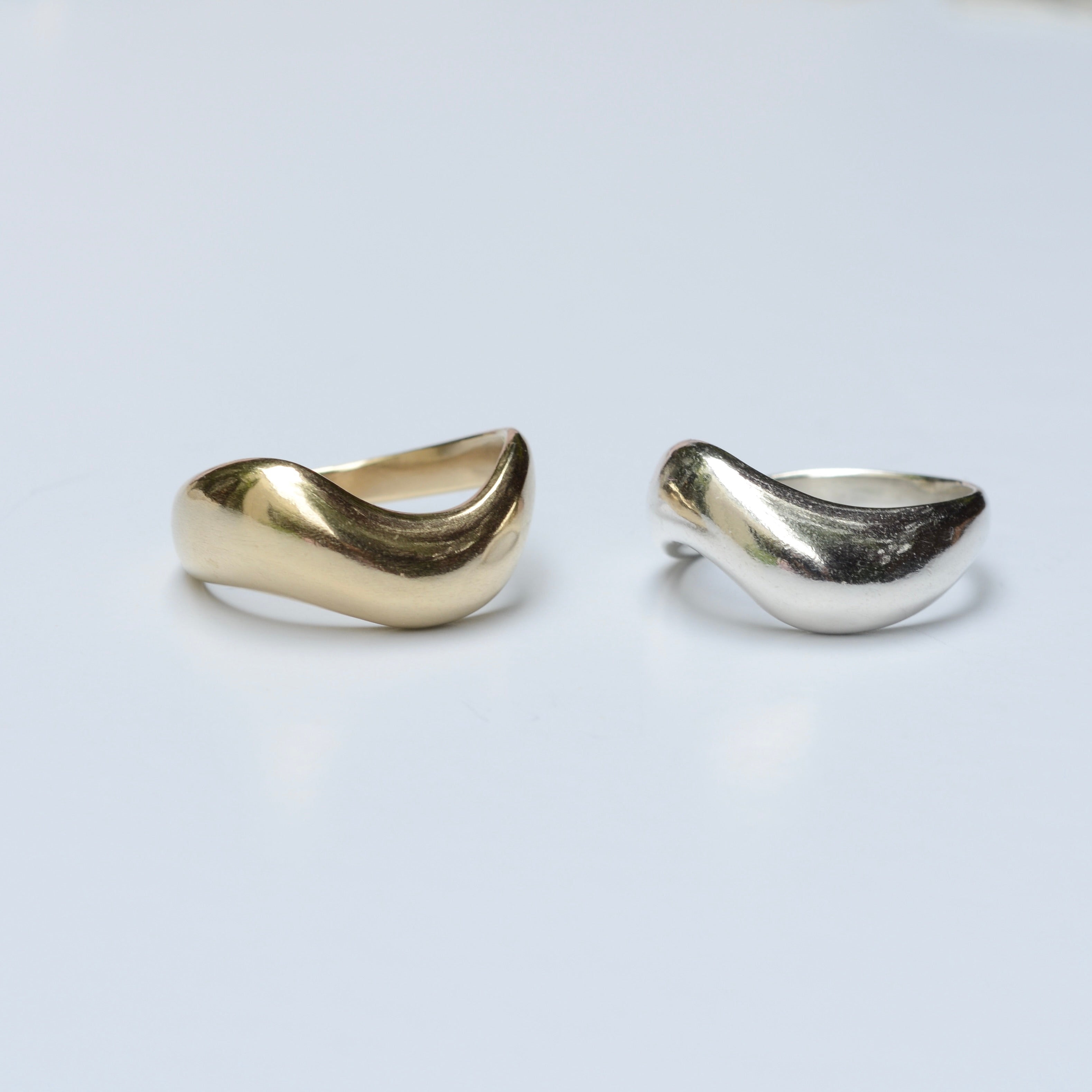 Two bronze and silver organic wavy rings on a light gray background