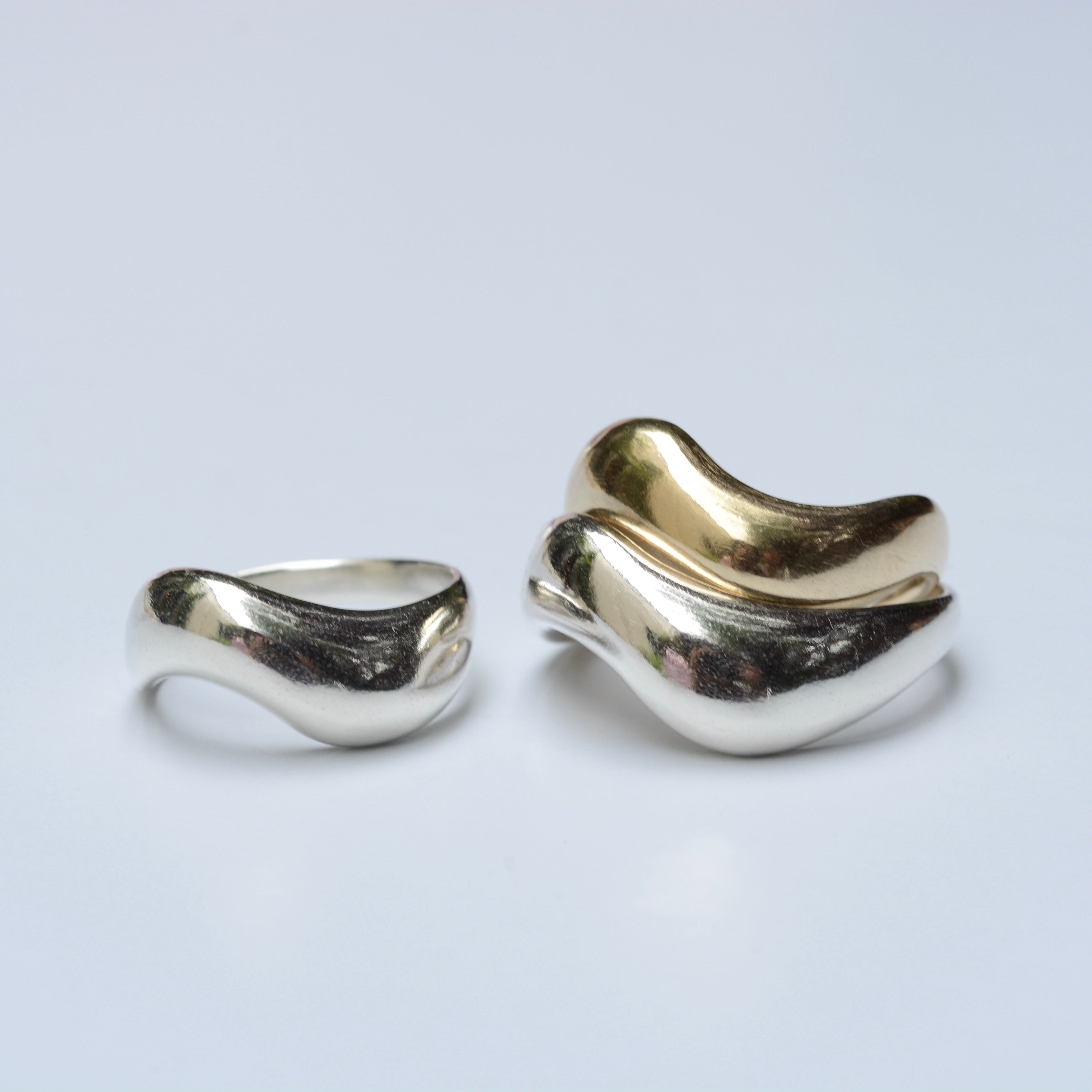 A stack of silver and bronze wide wavy rings with organic shapes on a light grey background
