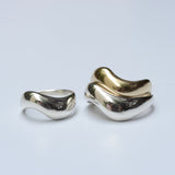 A stack of silver and bronze wide wavy rings with organic shapes on a light grey background