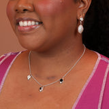 Woman wearing a silver charm necklace with oval pendants and mother of pearl, black onyx, and ying yang stones.