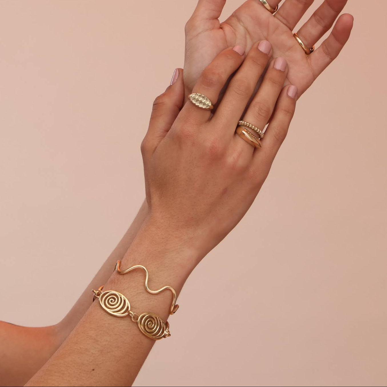 Gold jewelry including rings and bracelets on a hand against a beige background