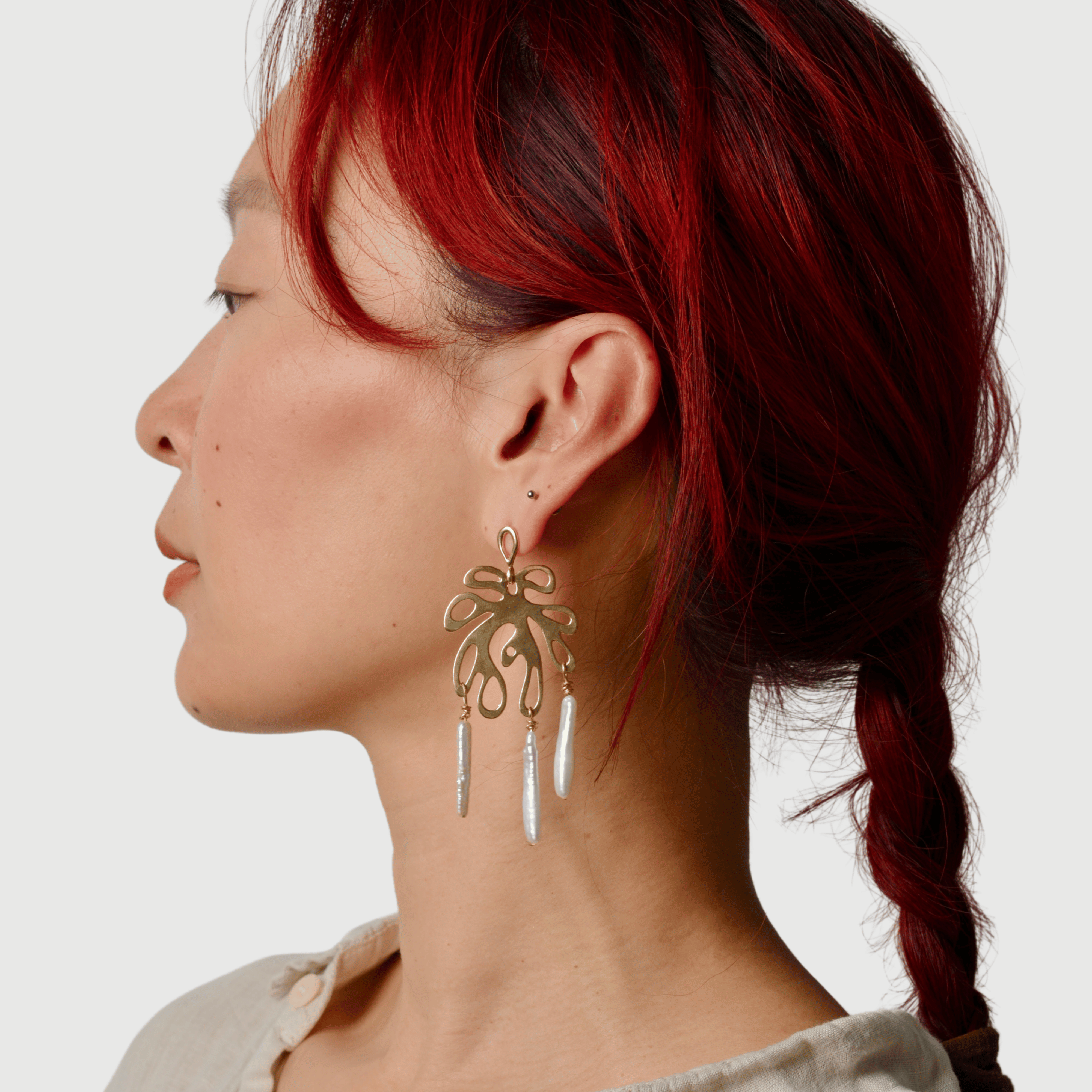Woman with red hair wearing a bronze leaf shaped statement earring with pearls against a white background
