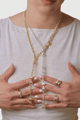 Person wearing two long necklace with bronze and silver chains, holding it with both hands that have wavy stacked rings on them.