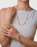 Woman wearing a silver necklace, bracelet, and ring on a plain background