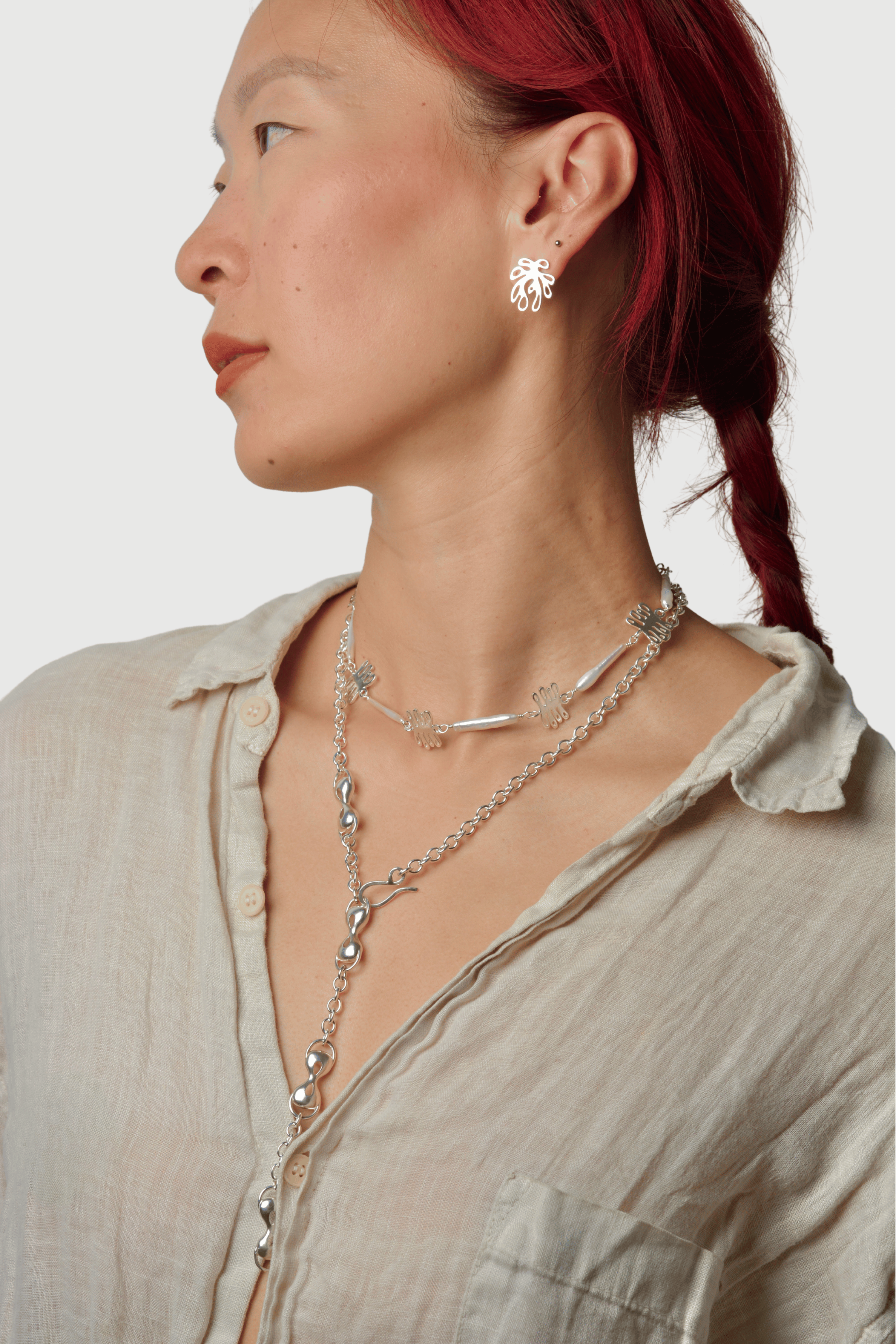 Woman wearing a silver necklace and earrings with a neutral background