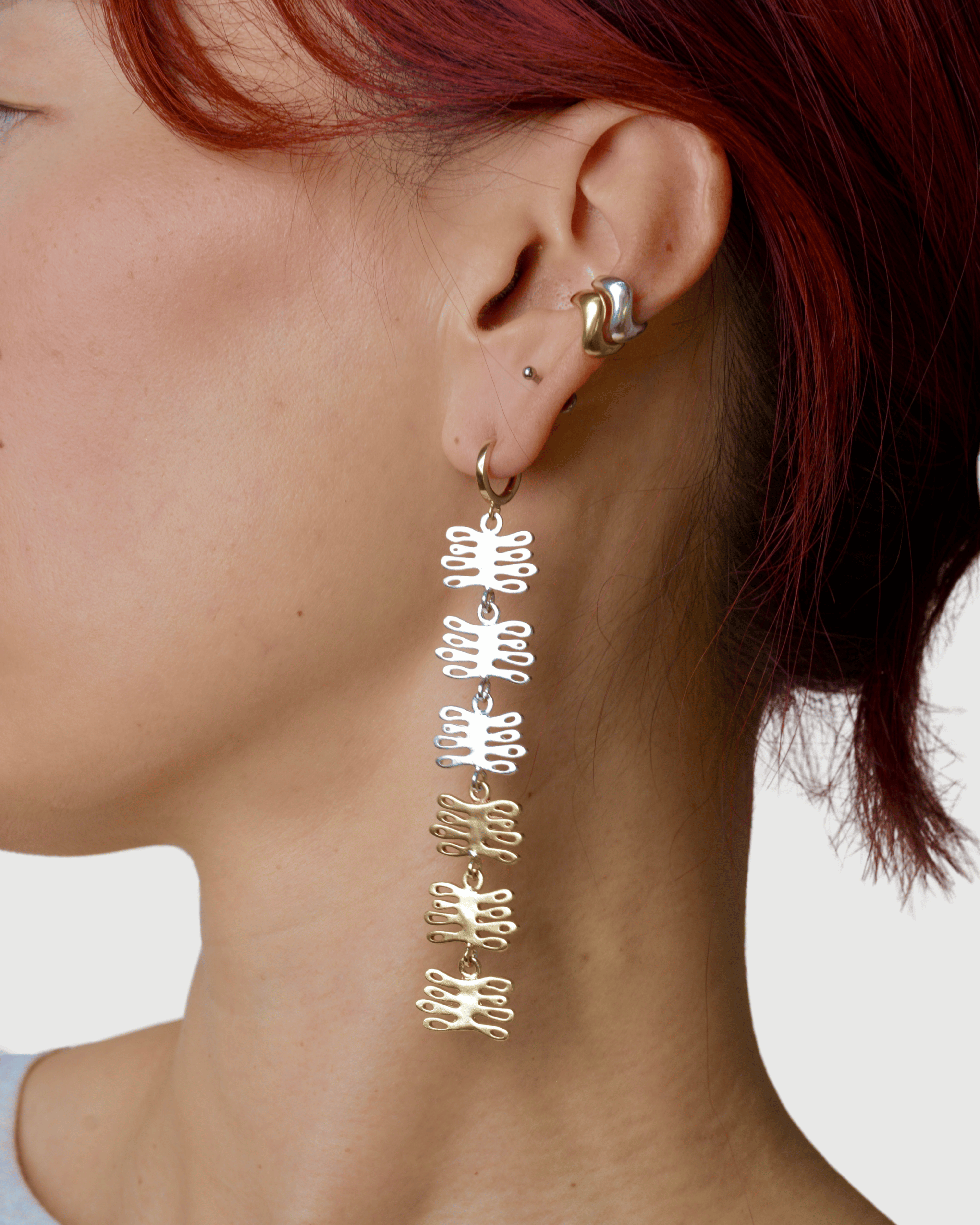 Person wearing long mixed metal earrings with coral shaped charms a plain background