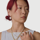 Woman wearing bronze coral shaped huggie earrings and other jewelry on a plain background
