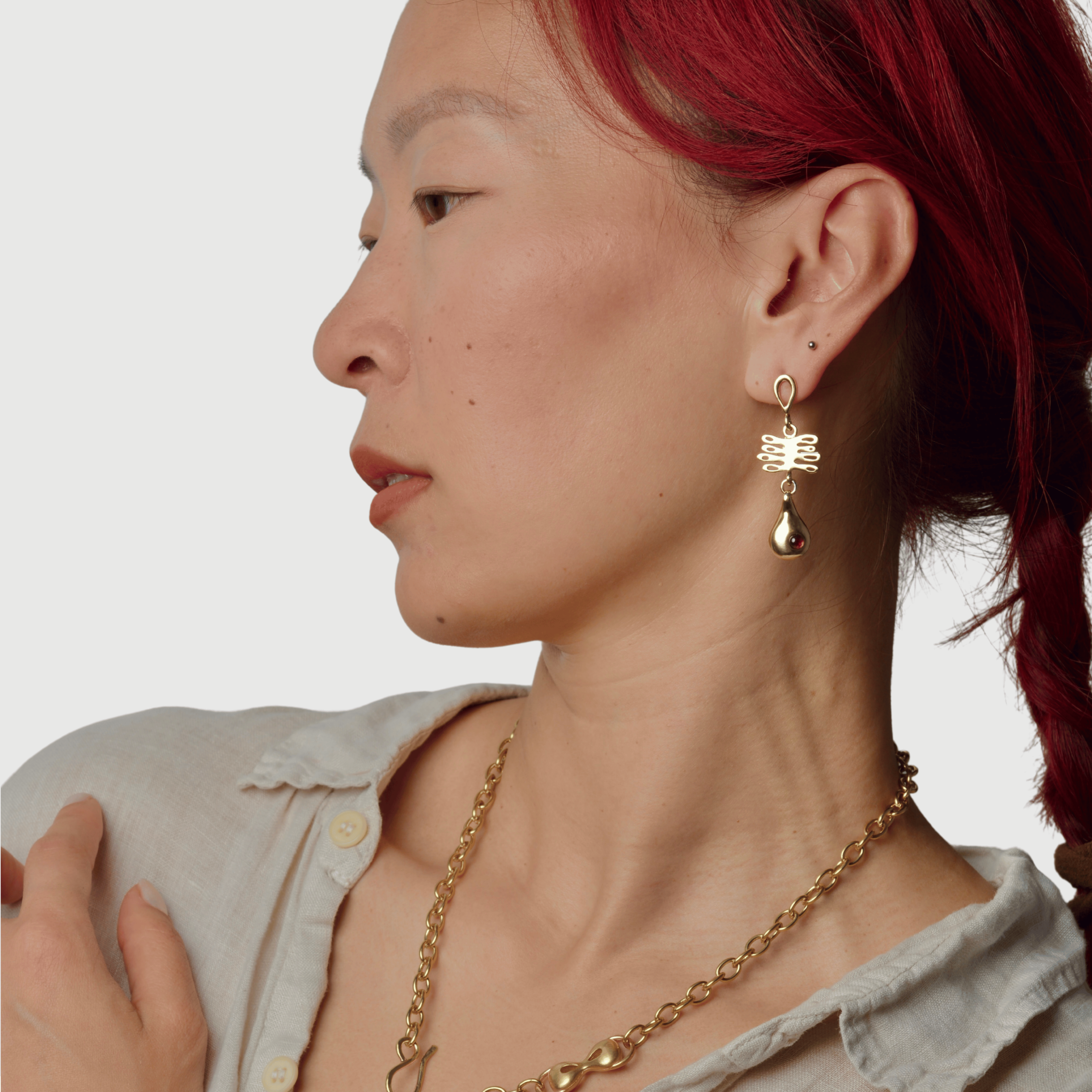 Woman wearing dangly bronze earrings with coral shaped pendant and droplet piece with a red garnet