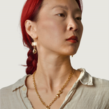 Woman wearing a gold necklace and bronze plant earrings against a neutral background