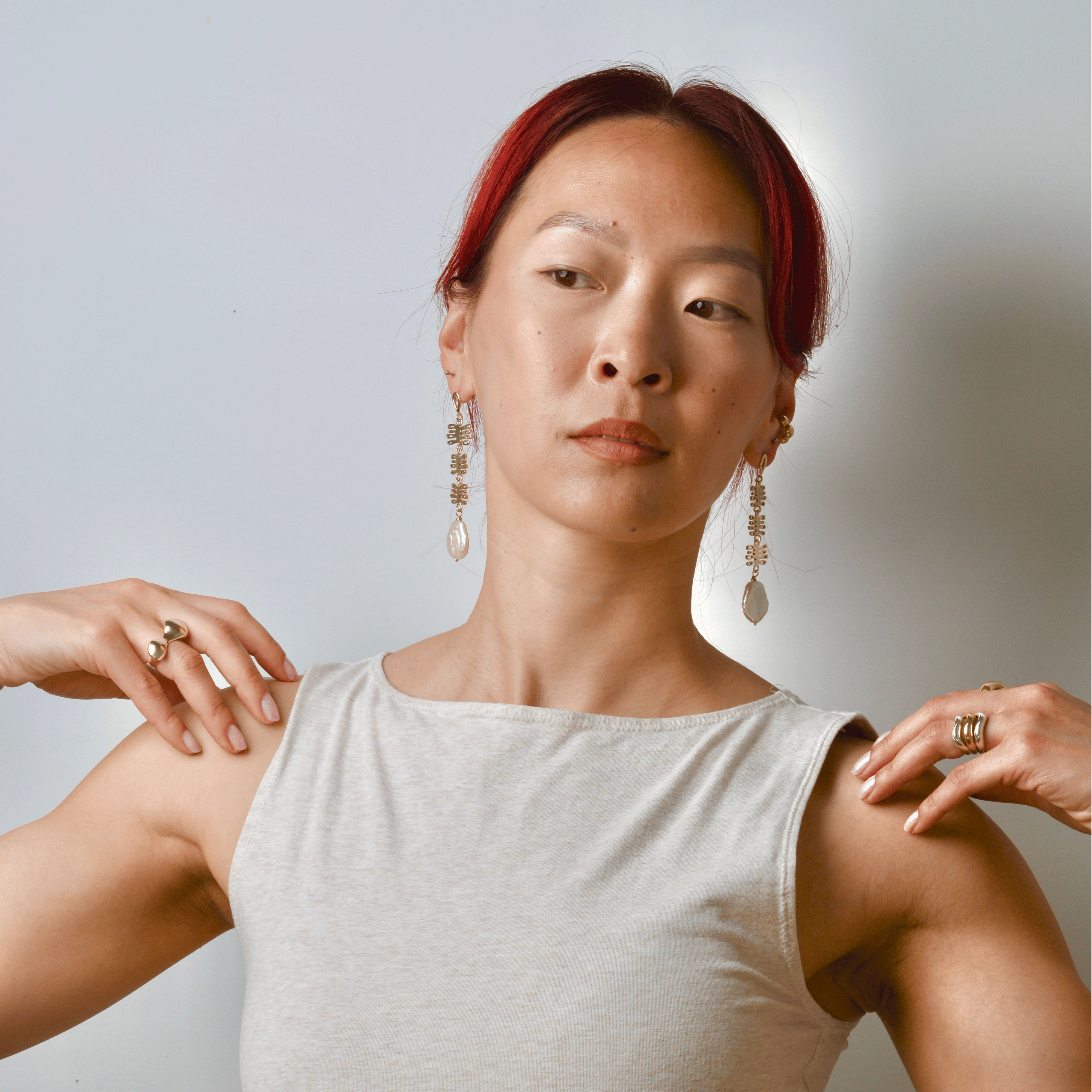 Woman wearing touching her shoulders modeling earrings that are bronze dangles with coral shaped charms and a pearl wearing a white sleeveless top against a plain background