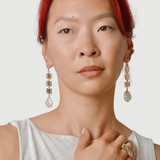 Woman with red hair wearing bronze coral shaped dangle earrings with pearls at the end and a white tank top on a plain background