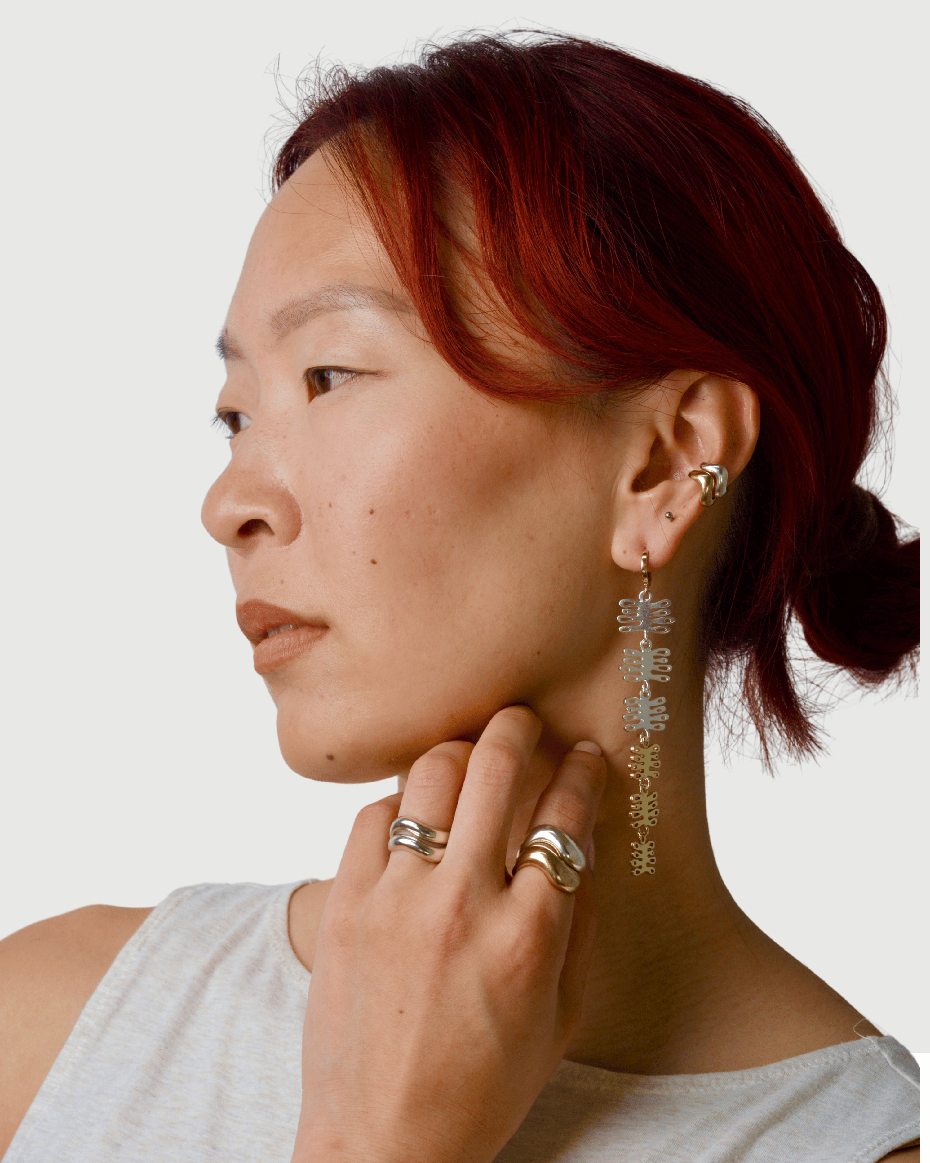 Woman wearing mixed metal earrings with plant charms, ear cuffs and wavy rings on a white background