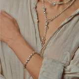 Person wearing a silver  unique link necklace and bracelet on a neutral background