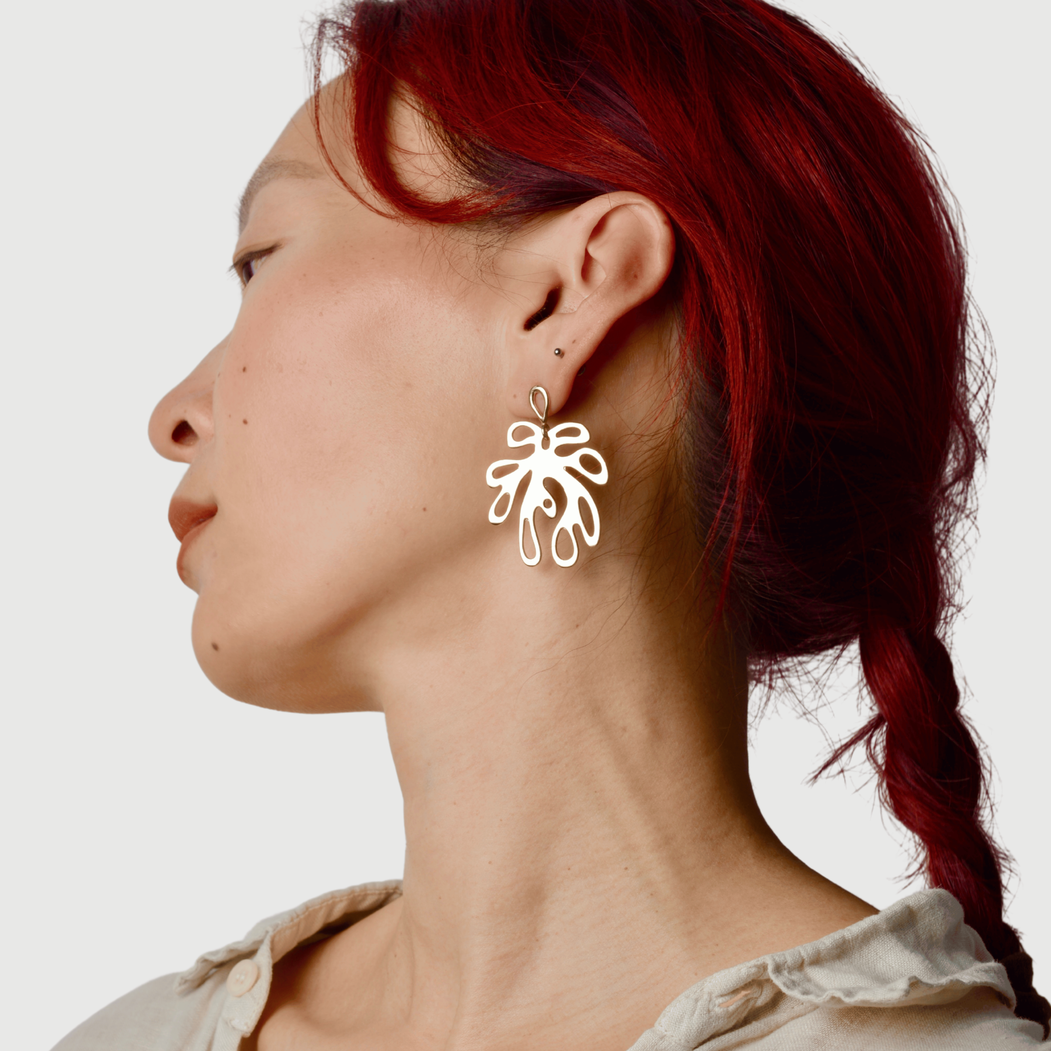 Woman wearing a leaf-shaped earring against a plain background