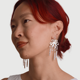 Woman wearing large leaf shaped silver earrings with pearls against a neutral background