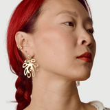 Close-up of a person wearing bronze leaf shaped earrings with a plain background