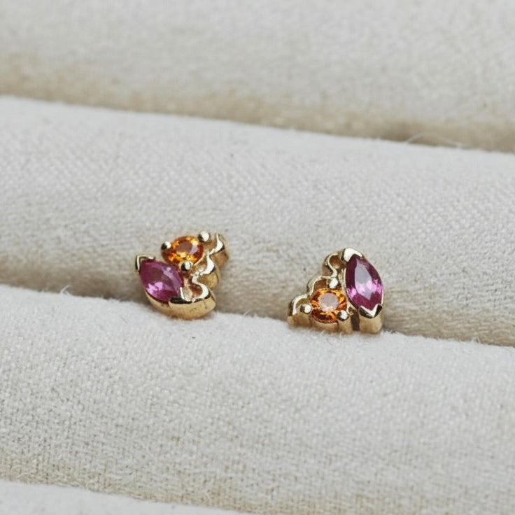 Pair of gold earrings with pink and orange gemstones on a cream cushion