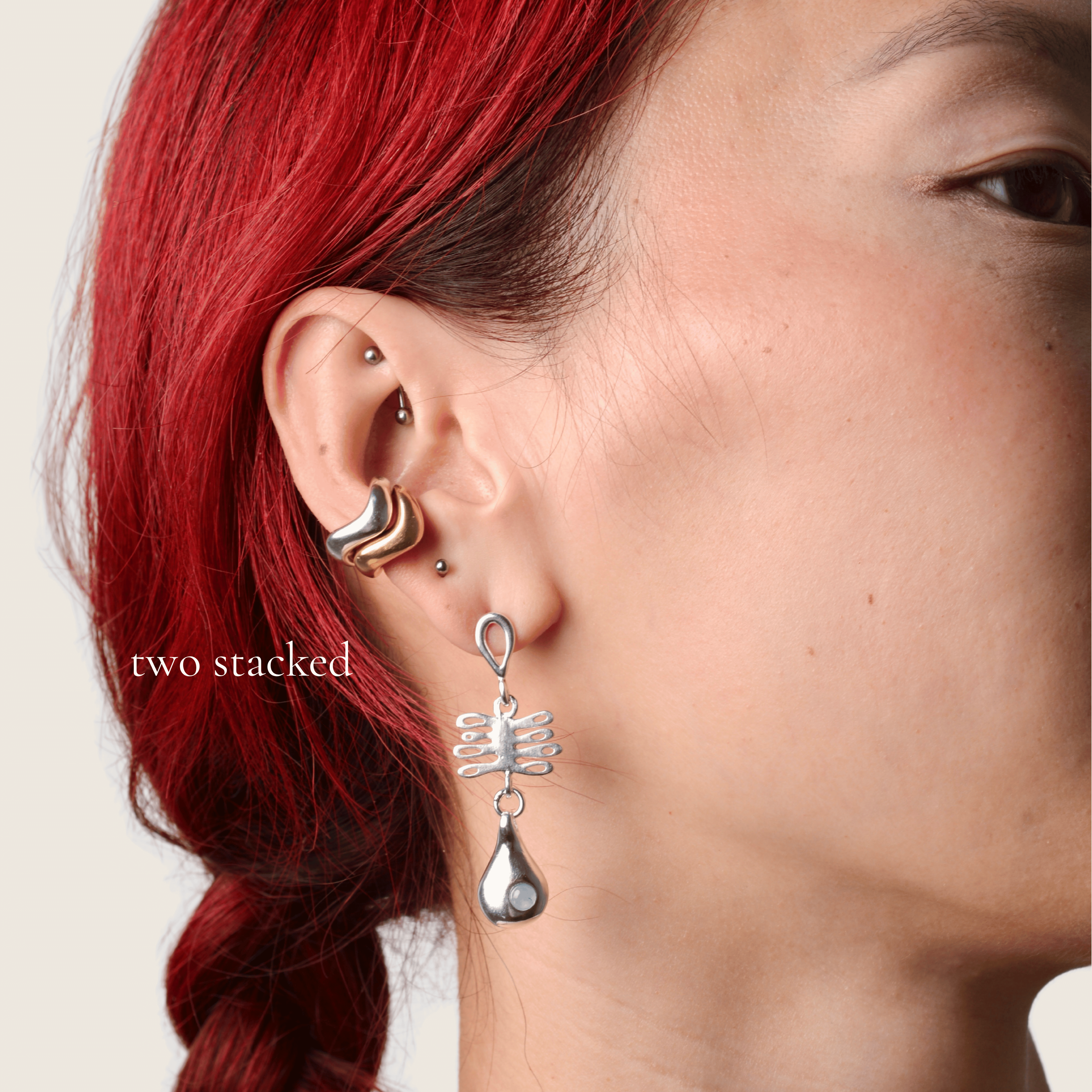 Close up of a woman wearing two wavy cuffs stacked together and another dangling silver earring 