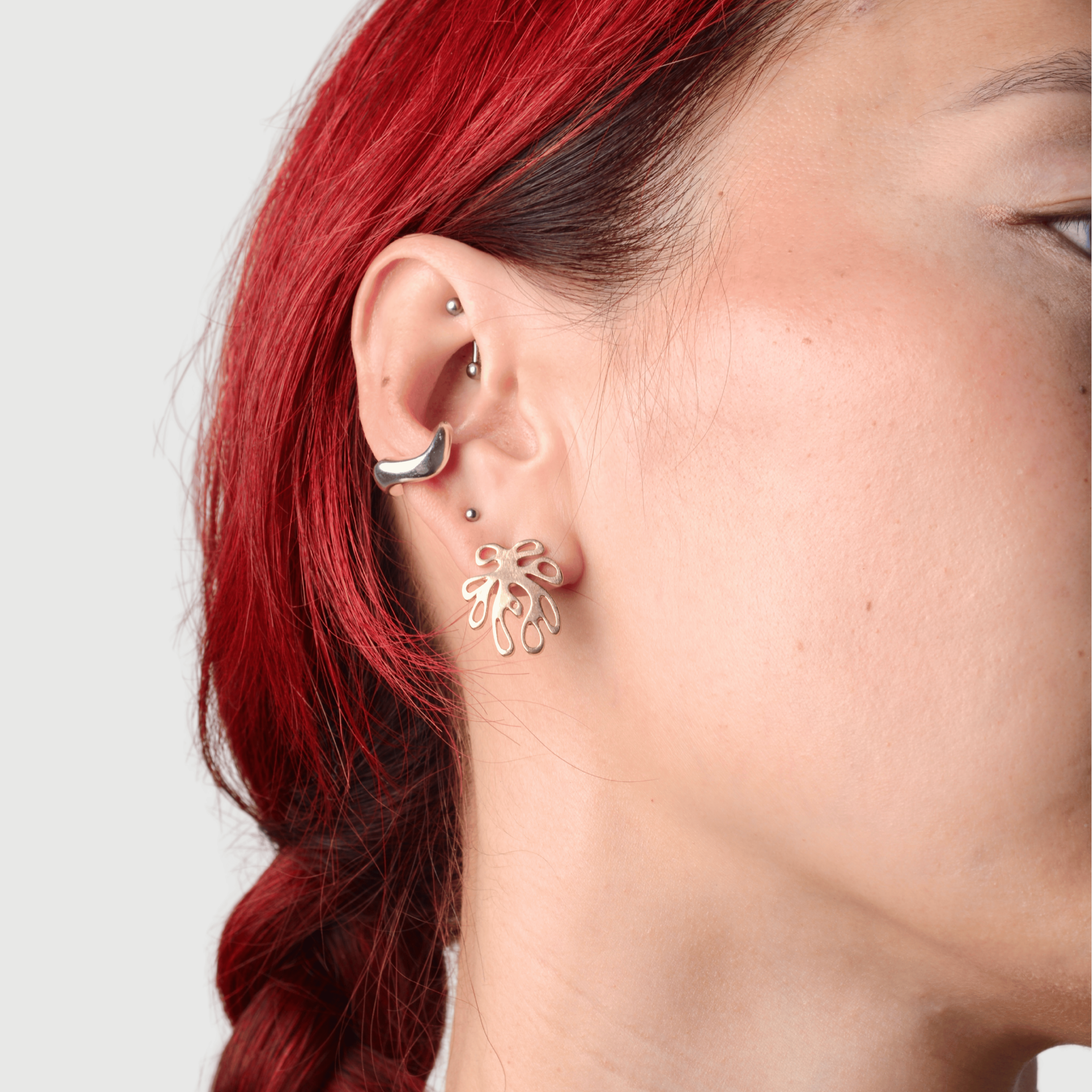 Close  up of a woman wearing a silver wavy ear cuff and a post of a coral shaped earrings