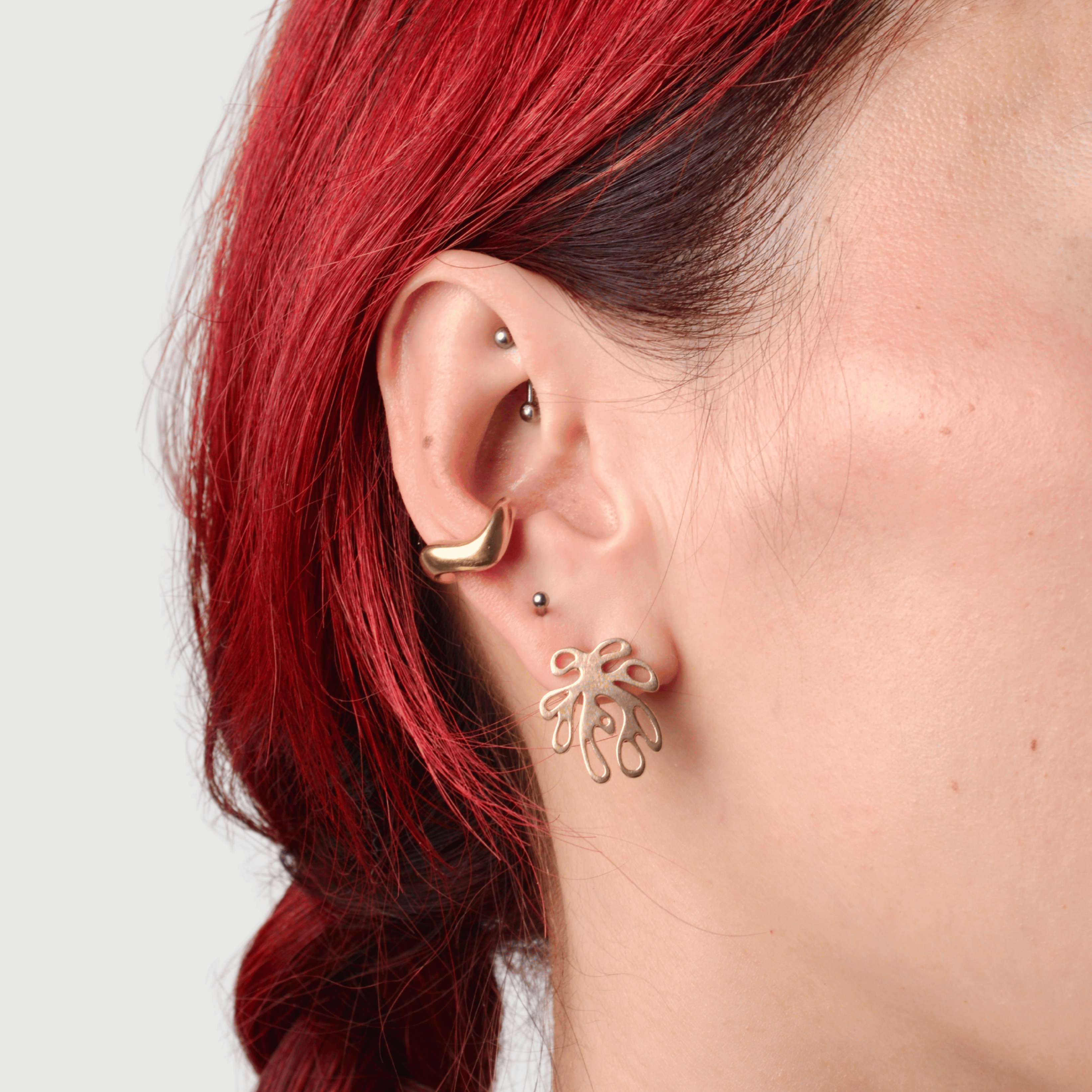 Close up of an ear wearing a bronze wavy ear cuff and a post with a coral shaped pendant. 