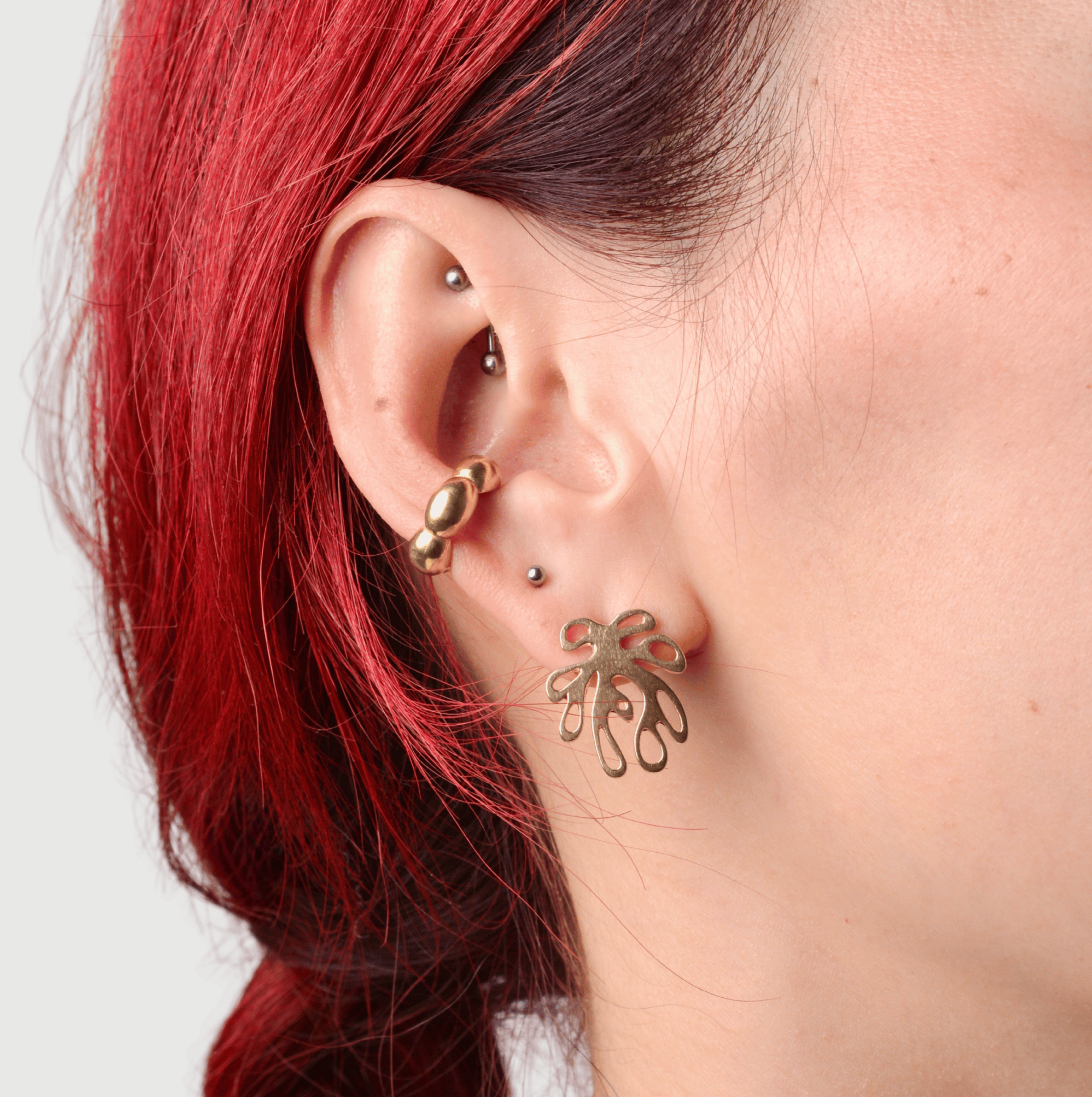Close-up of a person wearing bronze ear cuff and bronze post earring shaped like a plant with a red hair braid on a light background