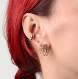 Close-up of a person wearing bronze ear cuff and bronze post earring shaped like a plant with a red hair braid on a light background