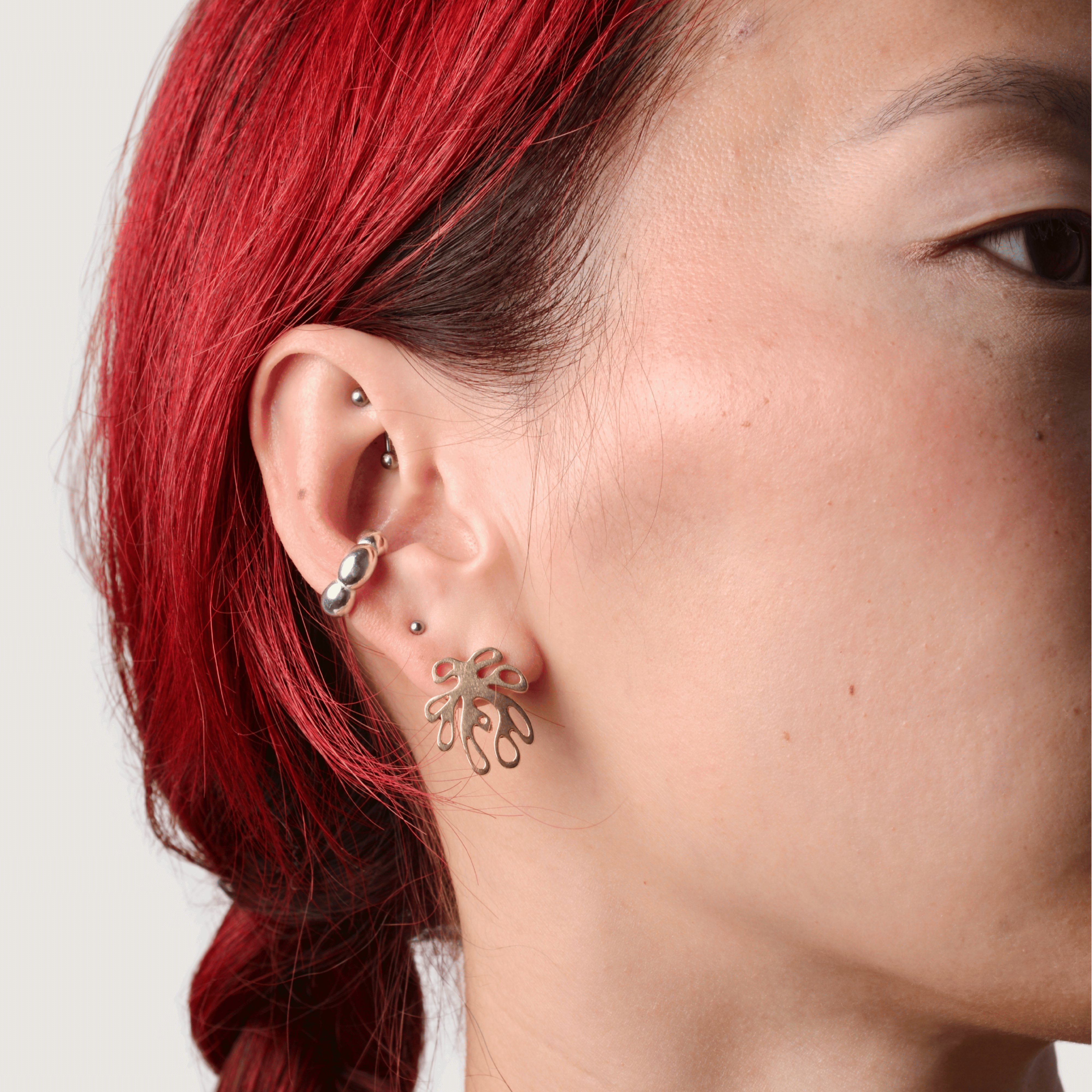 Person wearing silver bubble ear cuff and bronze coral shaped earring