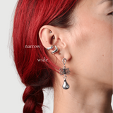 Close up of a woman wearing two silver wavy ear cuffs in narrow and wide and another silver dangle earring 