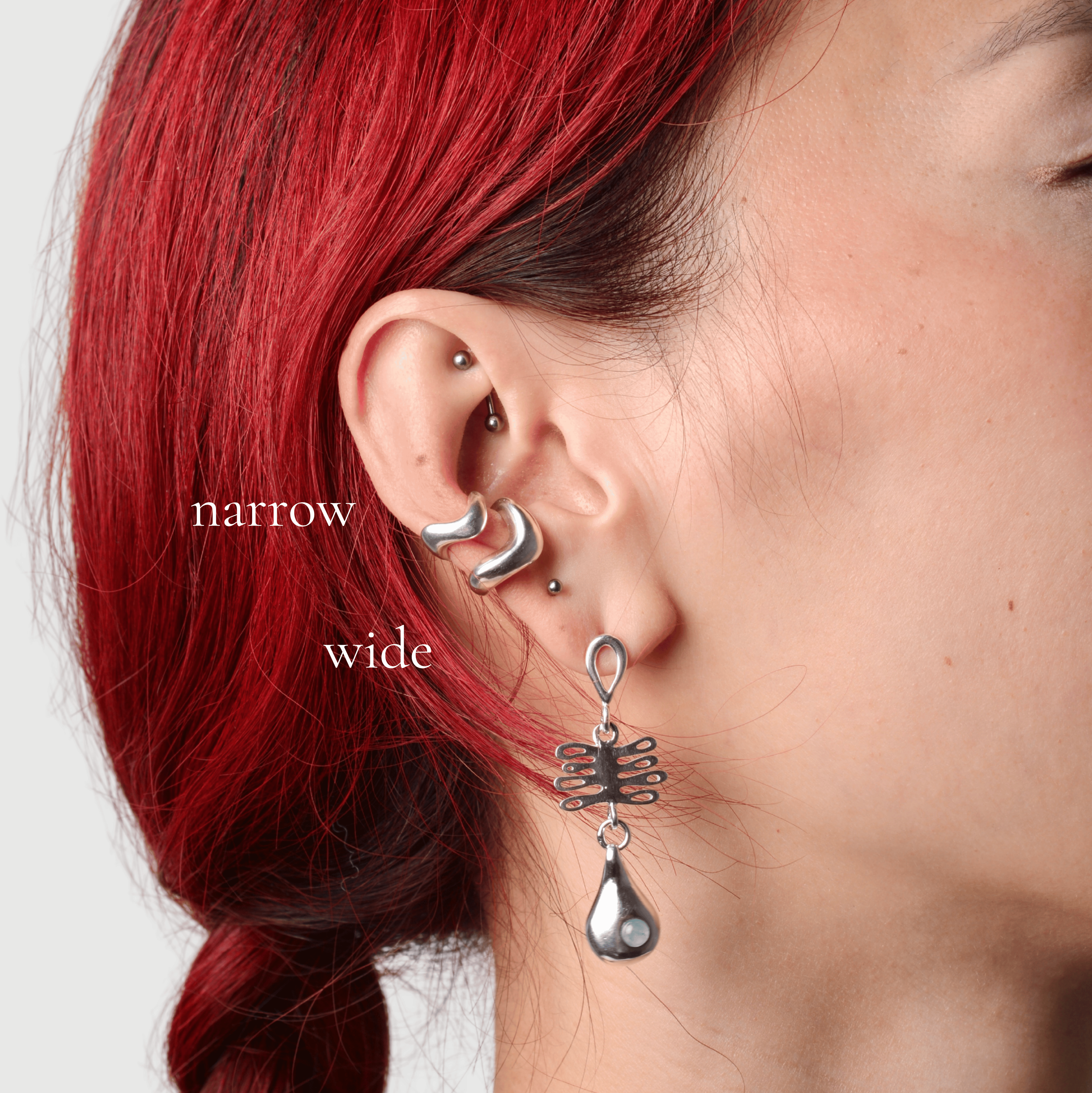Woman wearing two silver wavy ear cuffs in narrow and wide with a silver dangle earring that features a coral shaped charm and a droplet charm